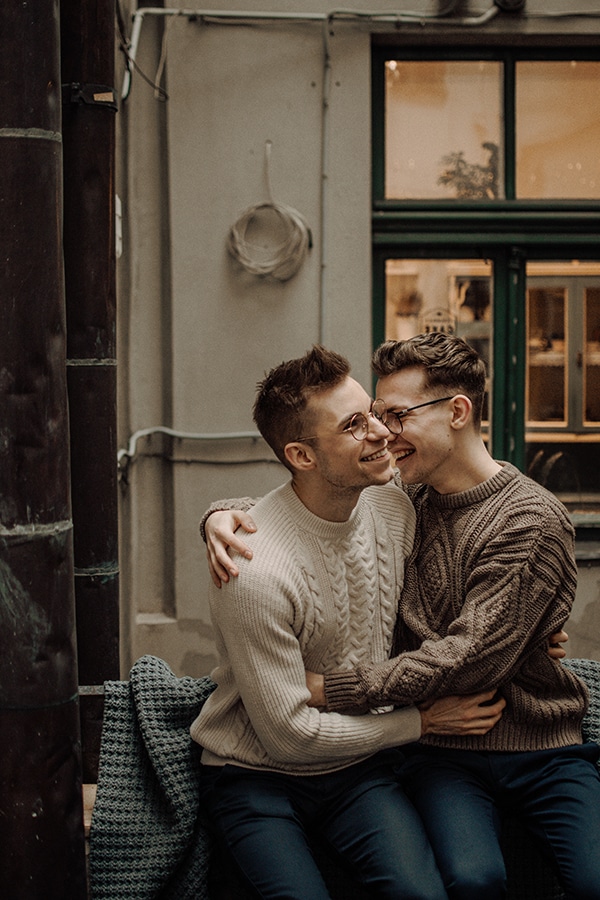 LGBTQ couple men laughing and hugging outside on bench