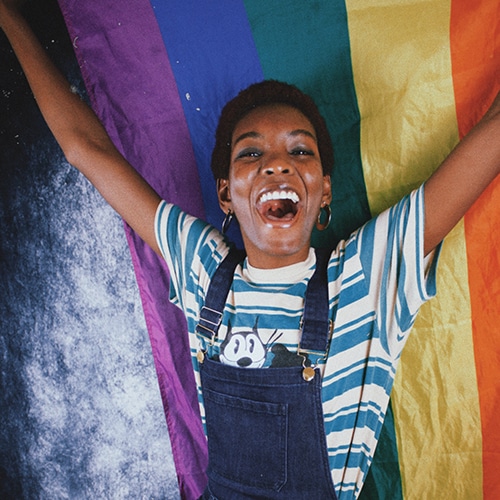 Person Smiling Cheering Arms Raised in front of LGBTQ flag